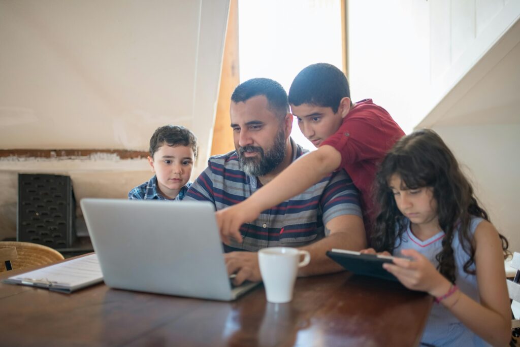 Father and children bonding over digital devices, fostering learning and togetherness.